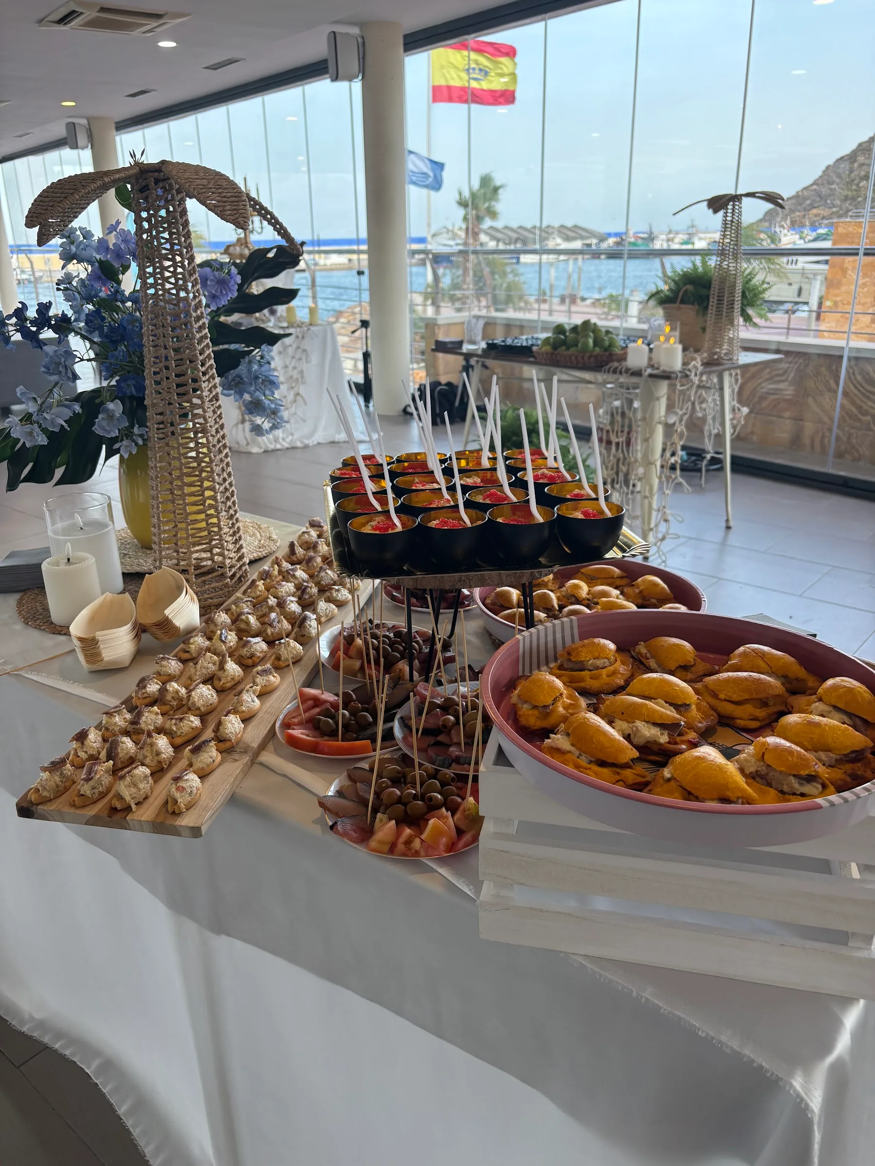 Eingedeckter Event-Tisch im Mazmara Sunset mit Canapés und Montaditos, und hinter dem Fenster der Hafen