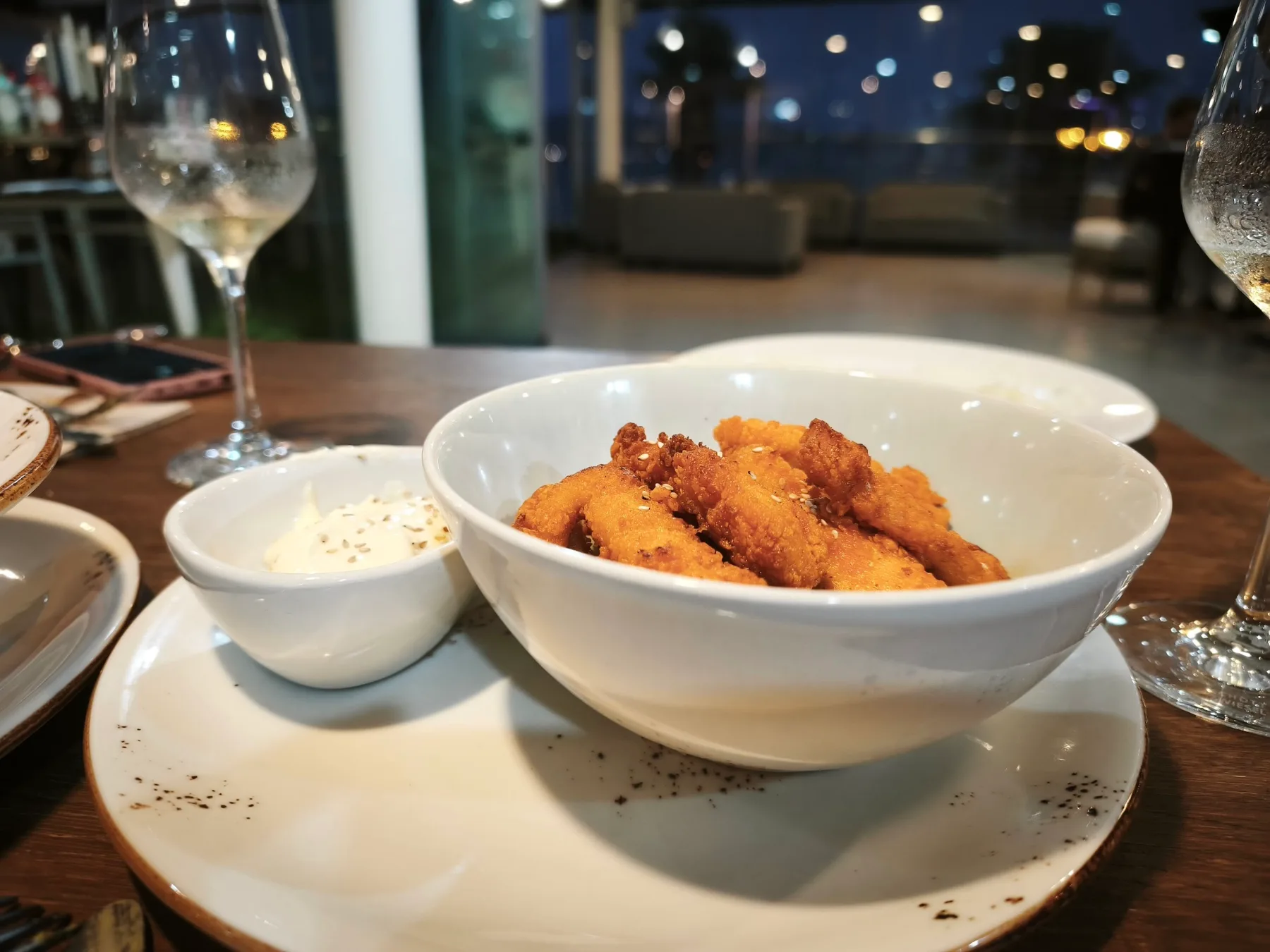 Eine Schale Tapas auf einem Tisch im Mazmara Sunset, dahinter die unscharfen Lichter des Hafens